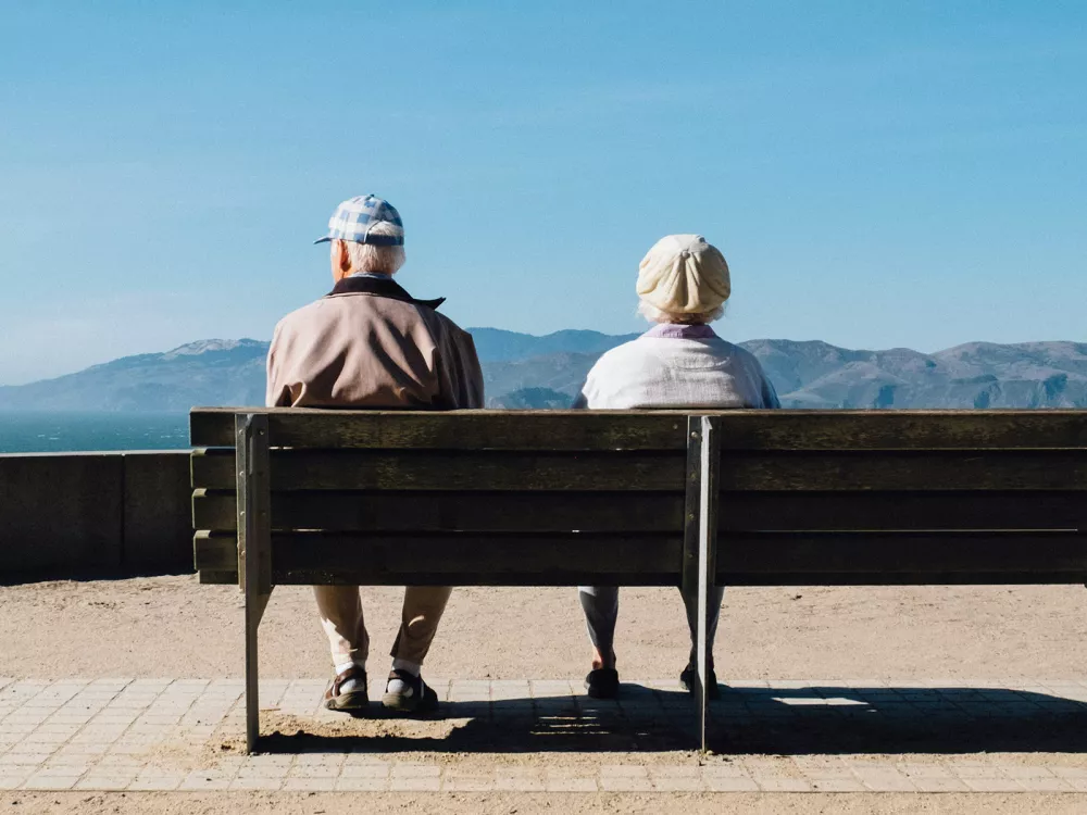 Photo de deux personnes âgées assises sur un banc face à un paysage de Genève. Illustration du vieillissement démographique