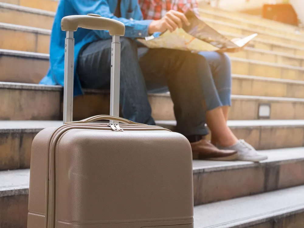 Un touriste consulte une carte de Genève avec sa valise posée pas loin de lui.